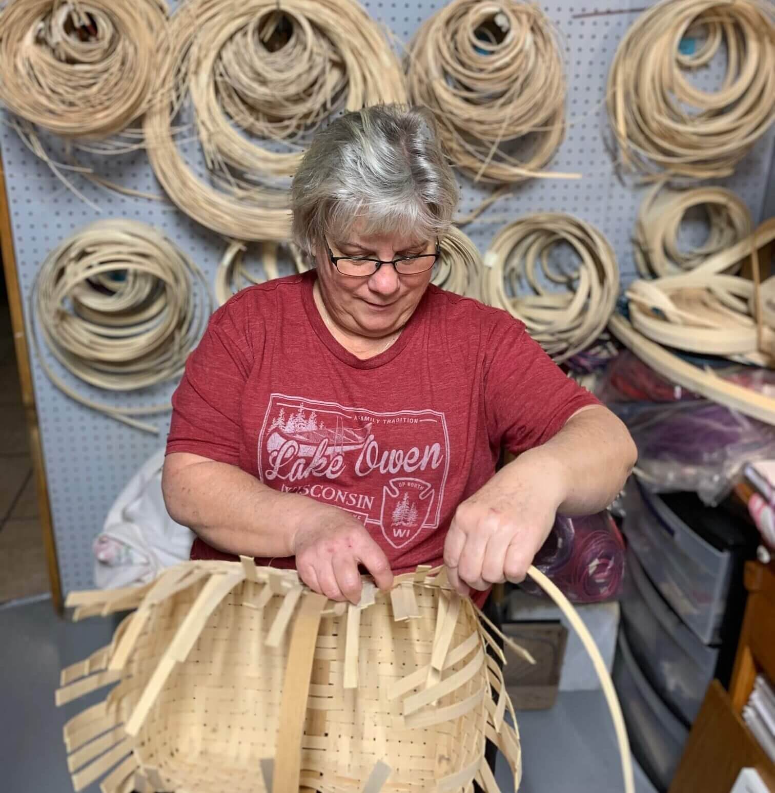 Barbara weaving a basket with a multiple rolls of reed in the background