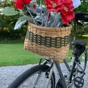 Homemade basket hanging on the front of a bicycle. The basket contains decorate flowers.
