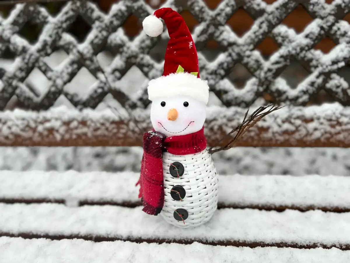 Woven snowman with a red hat and scarf sitting on a snow covered deck