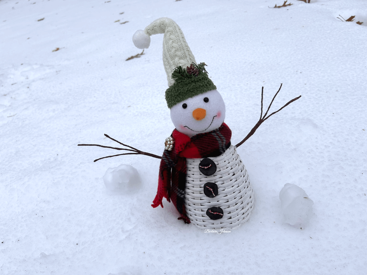 Snowman sitting outside in the snow has a red/black scarf on