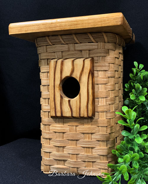 Woven birdhouse with wooden roof and wooden bottom.